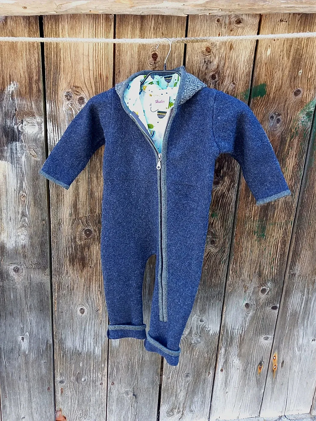 Kinder-Walkoverall in Blau an einer Holzwand